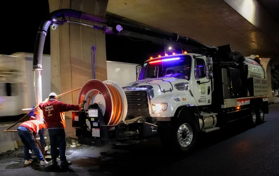 Men working with industrial cleaning machinery at night on urban streets.