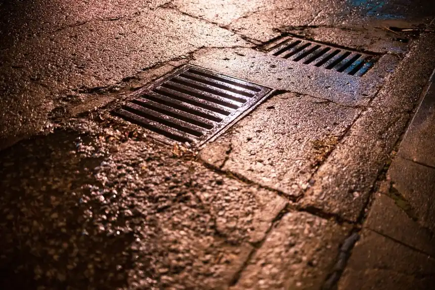Nighttime shot of wet asphalt road with drainage grates reflecting light.
